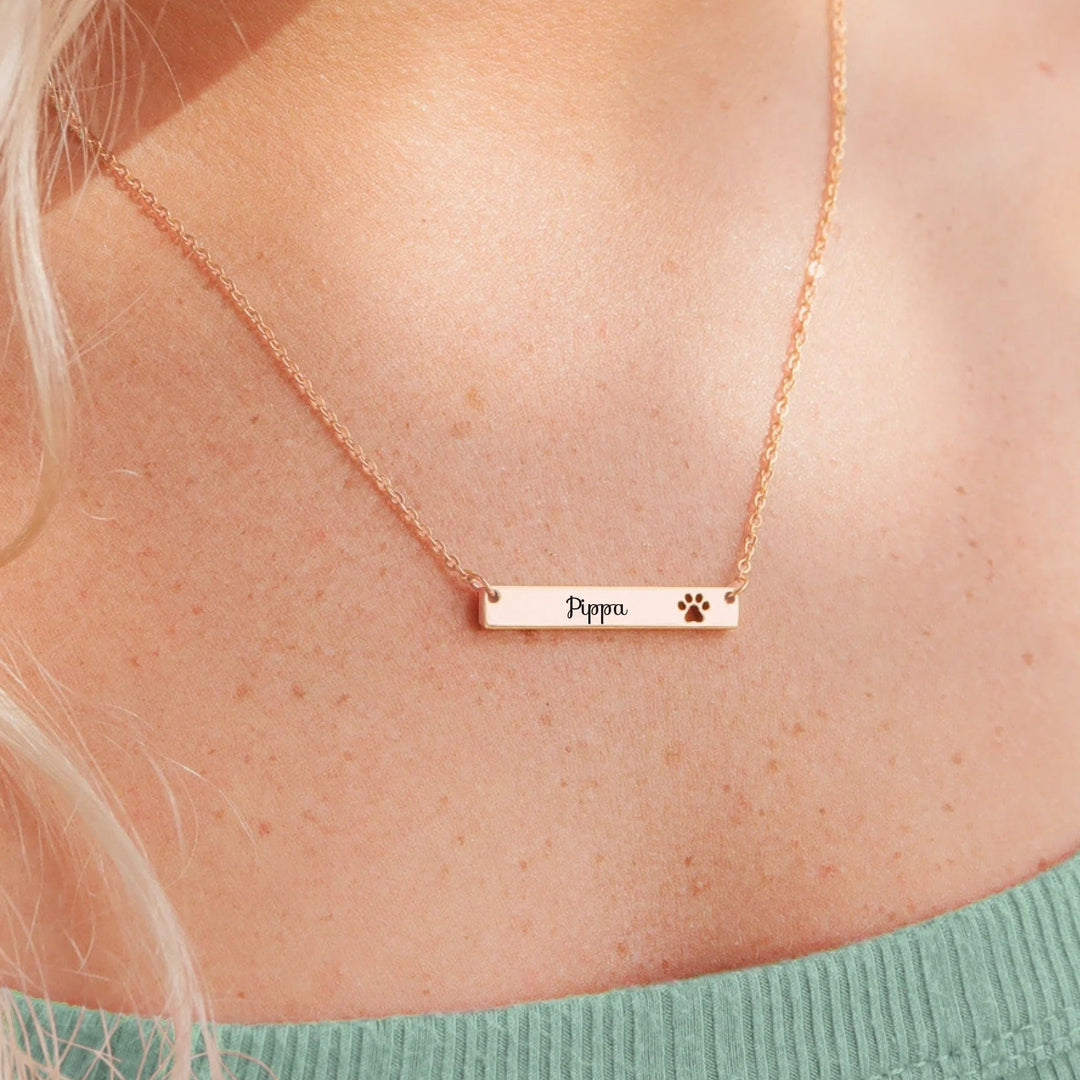 Rose gold necklace with engraved name and paw print on a person wearing a green top.